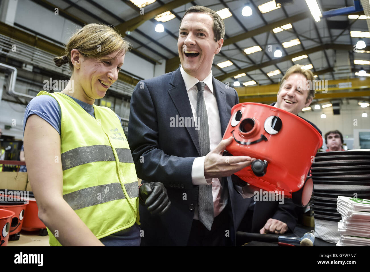 Schatzkanzler George Osborne teilt einen Witz und bewundert seine praktische Arbeit, nachdem er das Gesicht auf einem "Henry"-Vakuum zusammengelegt hat, das von der Fabrikarbeiterin Inga Ciplyte, 29, aus Exeter, während seines Besuchs in der Numatic-Fabrik gezeigt wurde, die die berühmte "Henry"-Vakuummarke in Chard, Somerset, produziert. Stockfoto