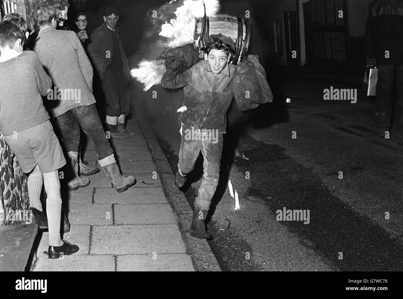 Tar Barrel Burning Ceremony - Ottery St Mary's. Ein Junge trägt ein Fass durch die Straße. Stockfoto