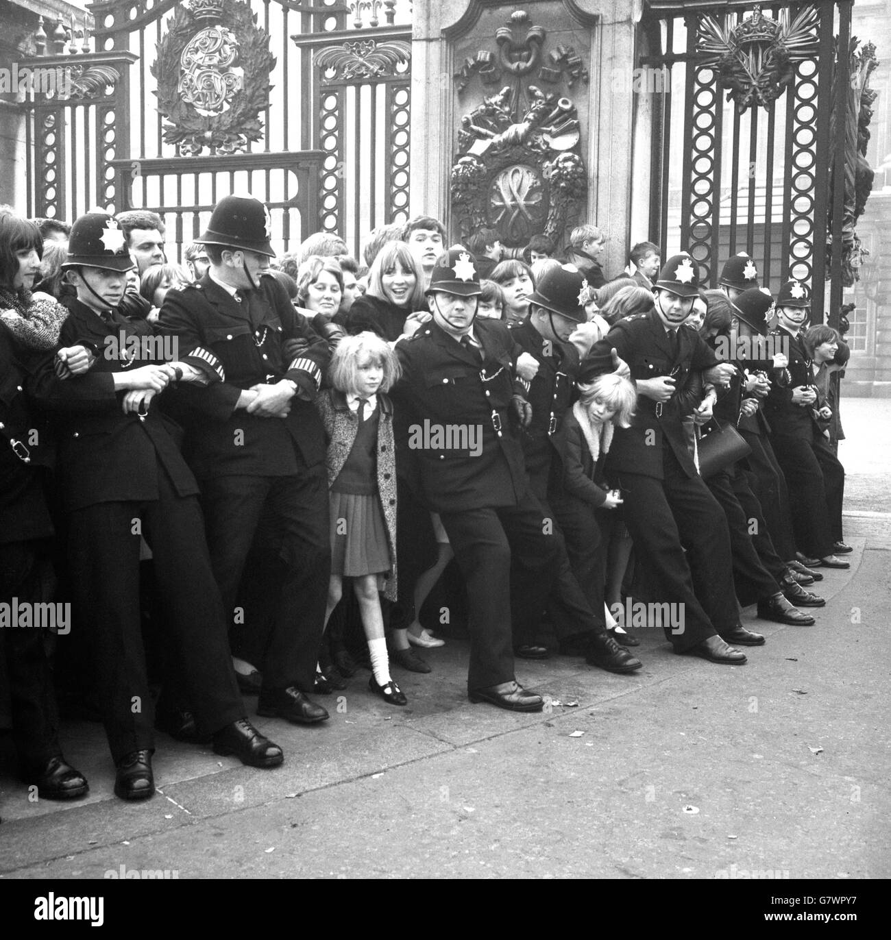 Die Polizei mit verbundenen Waffen hält die eifrigen Fans zurück, als die Beatles den Buckingham Palace verlassen, nachdem sie bei einer Investitur ihre Insignien als Mitglieder des Order of the British Empire von der Queen erhalten haben. Stockfoto
