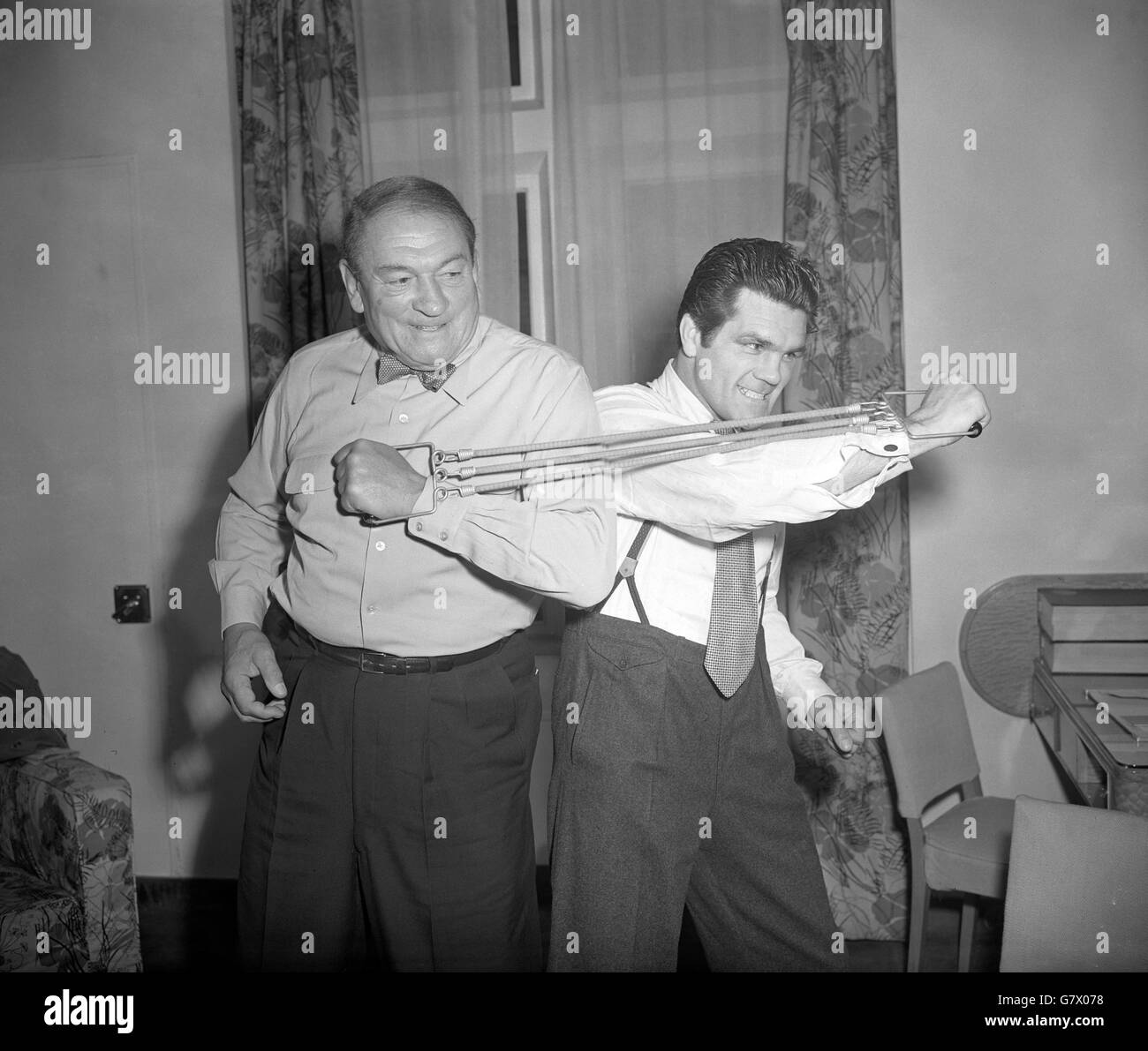 Trotz seiner 67 Jahre zeigt der Filmmusiker Victor McLaglan (l.) dem jungen Mann, dem ehemaligen World Light Heavyweight Boxweltmeister Freddie Mills, dass er immer noch so hart ist wie der Beste von ihnen. Freddie, jetzt Boxpromoter, besuchte McLaglan im Savoy Hotel in London und forderte ihn zu einem „Duell“ mit Brustaufweitern heraus. Stockfoto