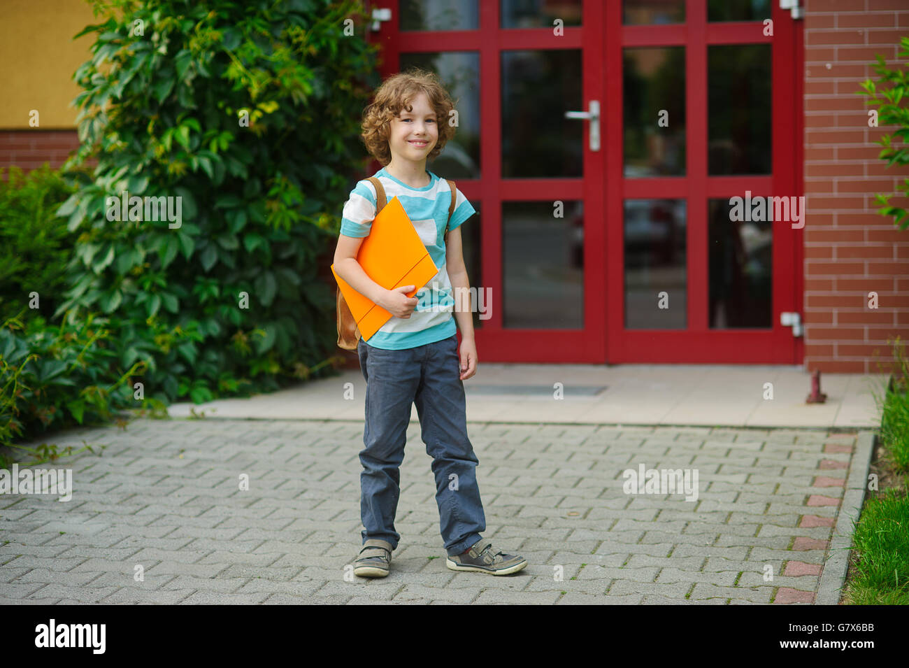 Die Schüler auf einem Schulhof. Pepe hat blondes lockiges Haar und ein schönes Gesicht. Hinter die Schultern auf die Pupille ein Ranzen, in Händen der Stockfoto