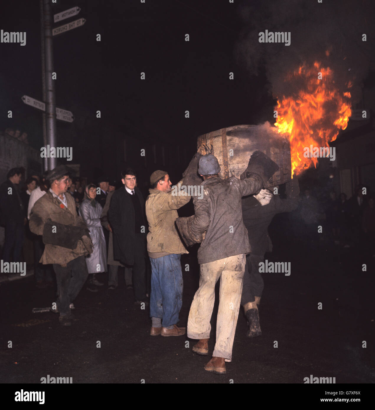 Männer tragen ein brennendes Fass durch die Straßen, während die Menschen darauf blicken. Stockfoto