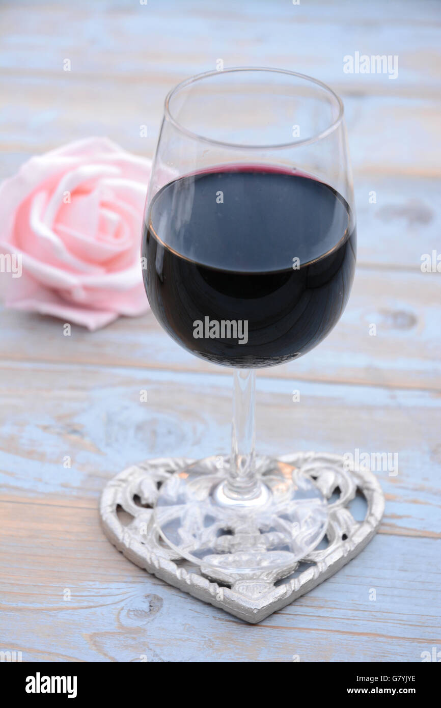 Flasche und Gss Rotwein auf einem hölzernen Hintergrund mit transparent weißer Stoff mit romantische Pastell rose Dekoration Stockfoto