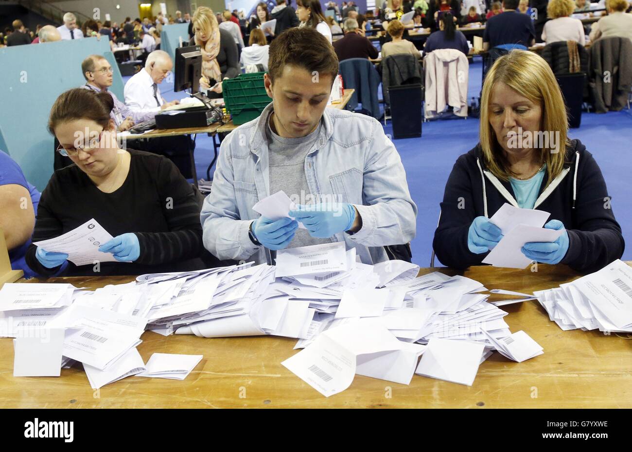 Die Mitarbeiter der Zählung tragen blaue Handschuhe, wenn sie bei der allgemeinen Wahlzählung für Wahlkreise in Glasgow in der Emirates Arena in Glasgow nach einer möglichen betrügerischen Abstimmung suchen. Stockfoto