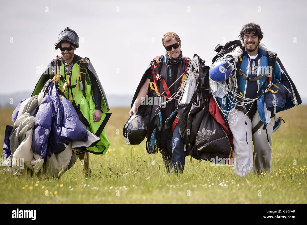 Wingsuit-Fallschirmspringer tragen ihre Fallschirme nach der Landung auf dem ersten FAI (World Air Sports Federation) anerkannten Wingsuit World Cup auf dem Flugplatz Netheravon bei Salisbury, Wiltshire. Stockfoto