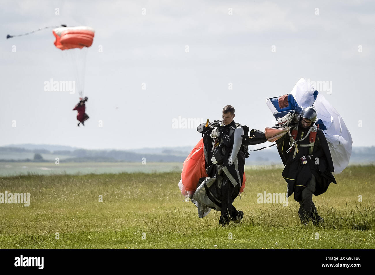 Wingsuit-Fallschirmspringer tragen ihre Fallschirme nach der Landung auf dem ersten FAI (World Air Sports Federation) anerkannten Wingsuit World Cup auf dem Flugplatz Netheravon bei Salisbury, Wiltshire. Stockfoto