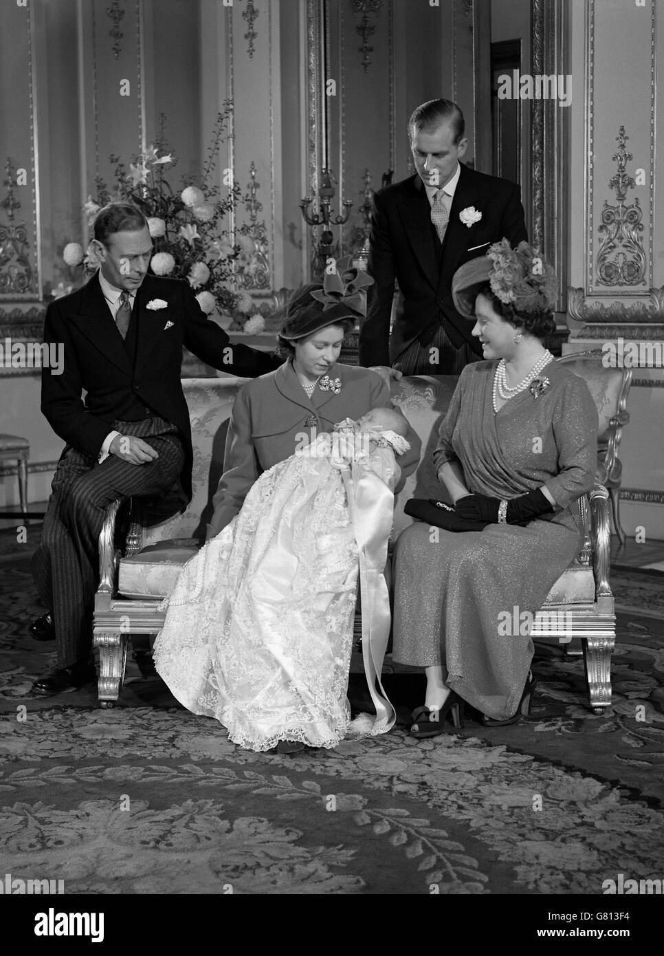 König George VI, links, der Herzog von Edinburgh, zurück, und Königin Elizabeth, rechts sehen auf als Prinzessin Elizabeth, Mitte, hält Prinz Charles nach seiner Taufe. Stockfoto