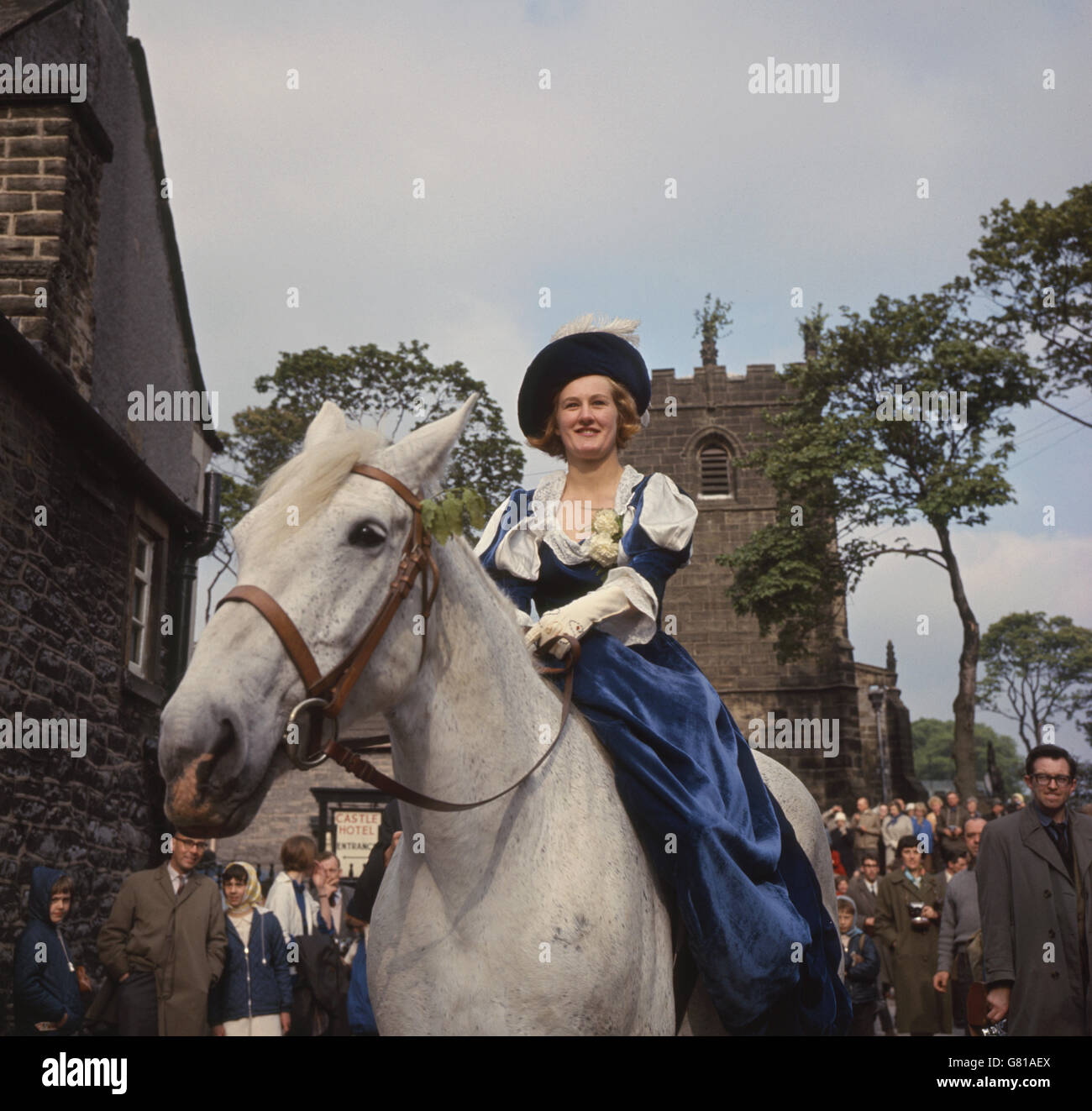 Beim Girlande Day „King“ wird seine Blumengirlande entfernt, während die „Queen“ zuschaut. Die Girlande wird dann auf die Kirchturmspitze gehisst. Peveril Castle ist im Hintergrund. Stockfoto