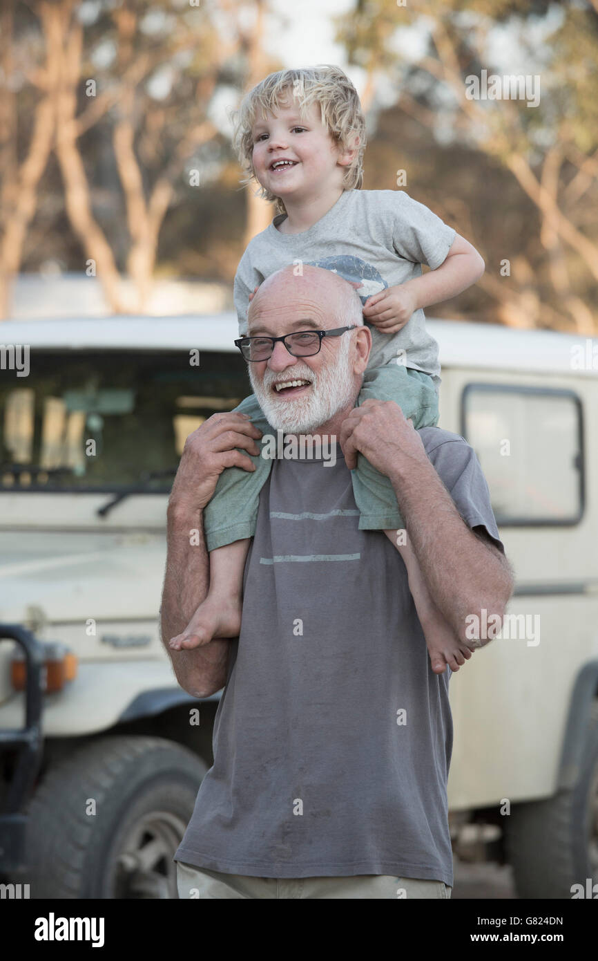 Glückliche Großvater tragen junge auf Schultern im freien Stockfoto