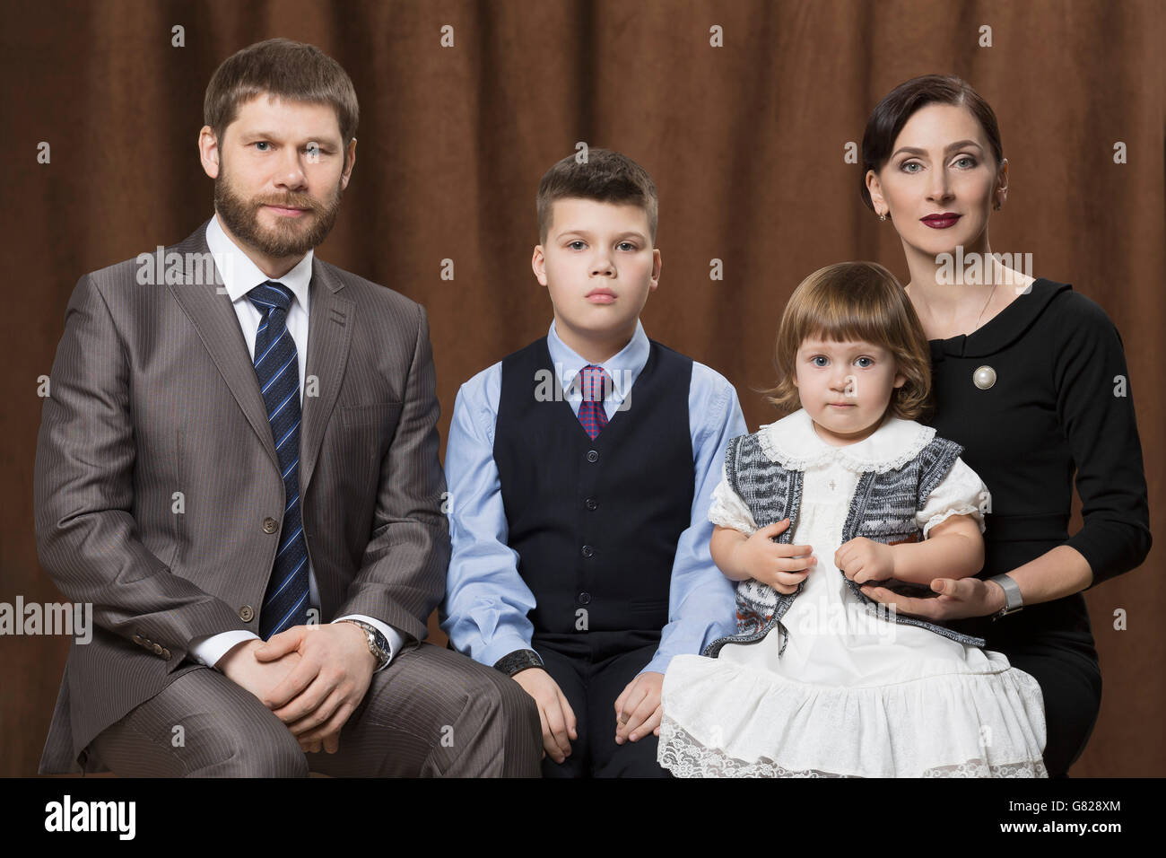 Porträt der Familie gegen braune Vorhänge im Studio sitzt Stockfoto
