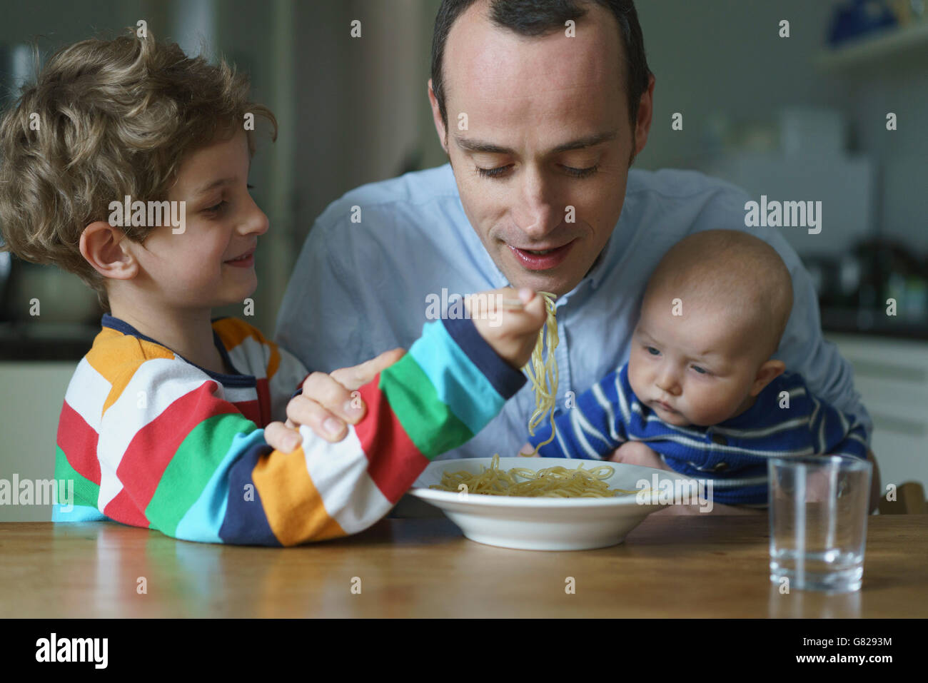 Junge Fütterung Nudeln, Vater mit Sohn am Tisch Stockfoto