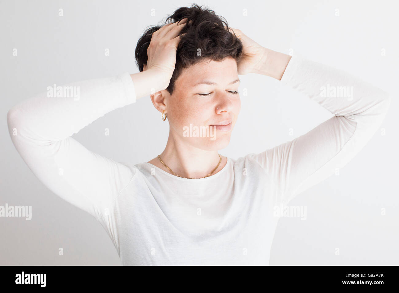 Entspannte Mitte Erwachsene Frau mit Händen im Haar vor weißem Hintergrund Stockfoto