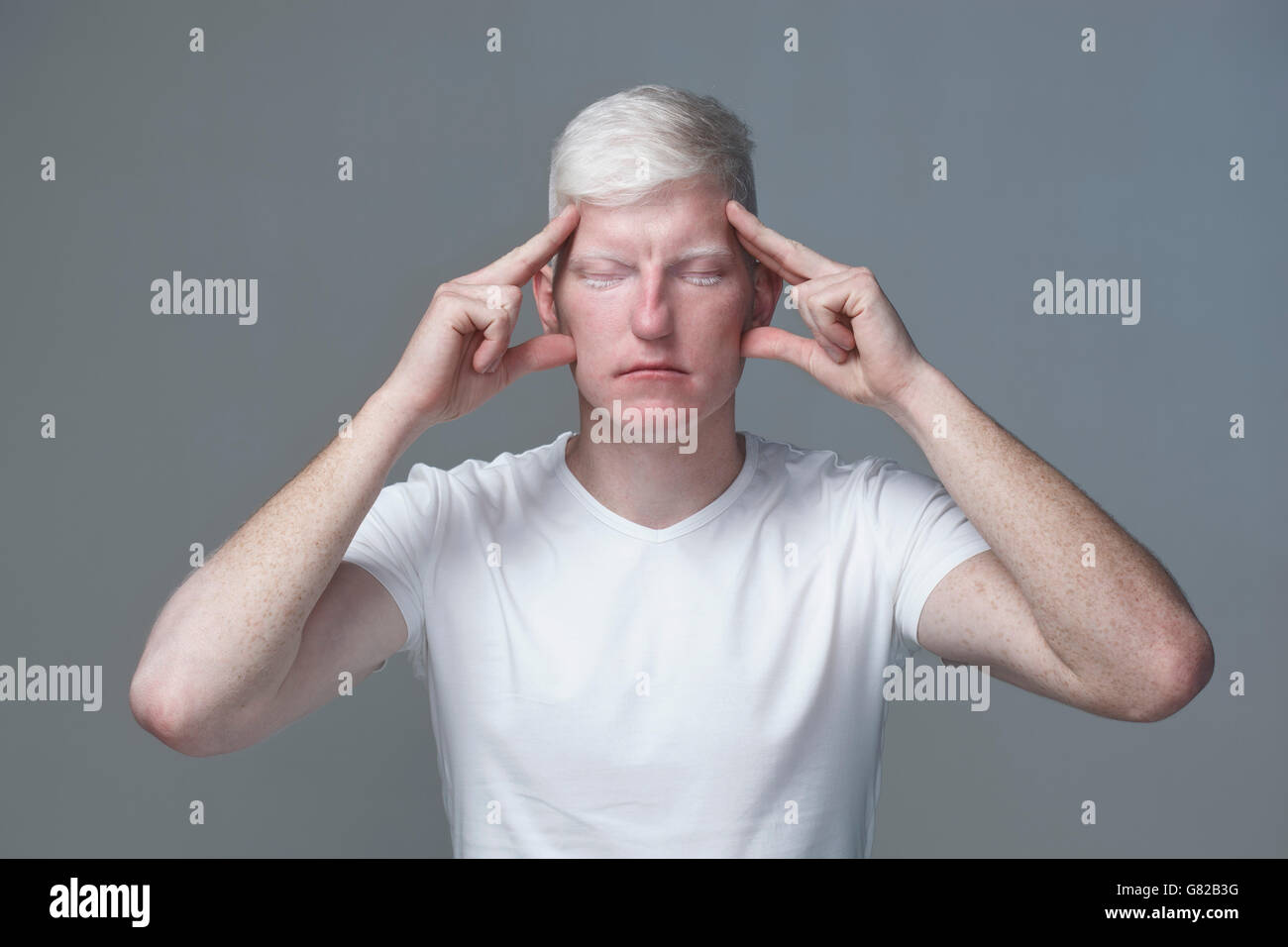 Porträt des jungen Mannes Fokussierung mit geschlossenen Augen vor grauen Hintergrund Stockfoto