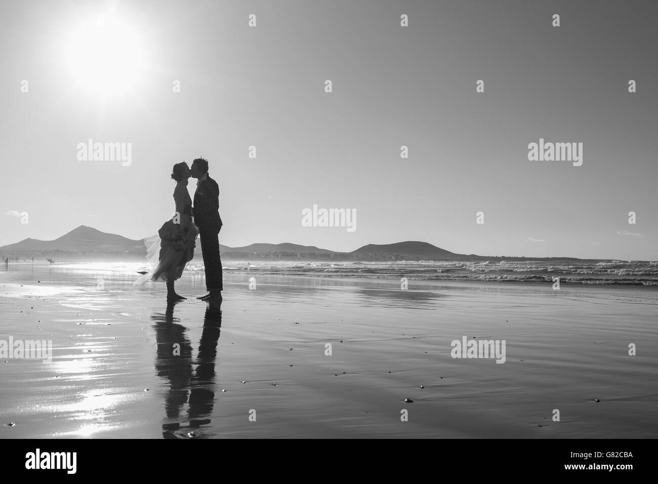Voller Länge Seitenansicht von Braut und Bräutigam küssen am Strand gegen klaren Himmel Stockfoto