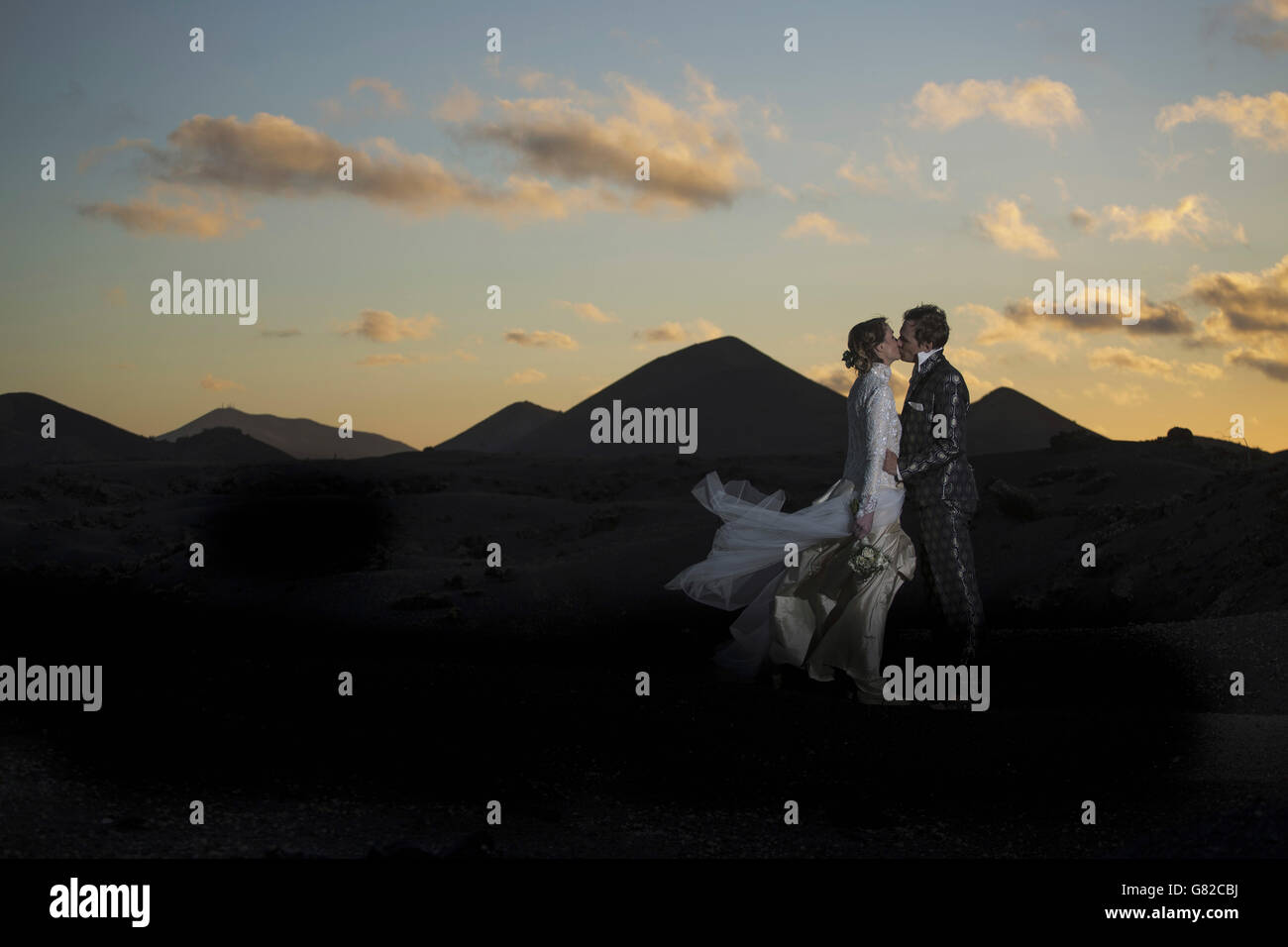 Voller Länge Seitenansicht von Braut und Bräutigam küssen auf vulkanische Landschaft bei Sonnenuntergang Stockfoto