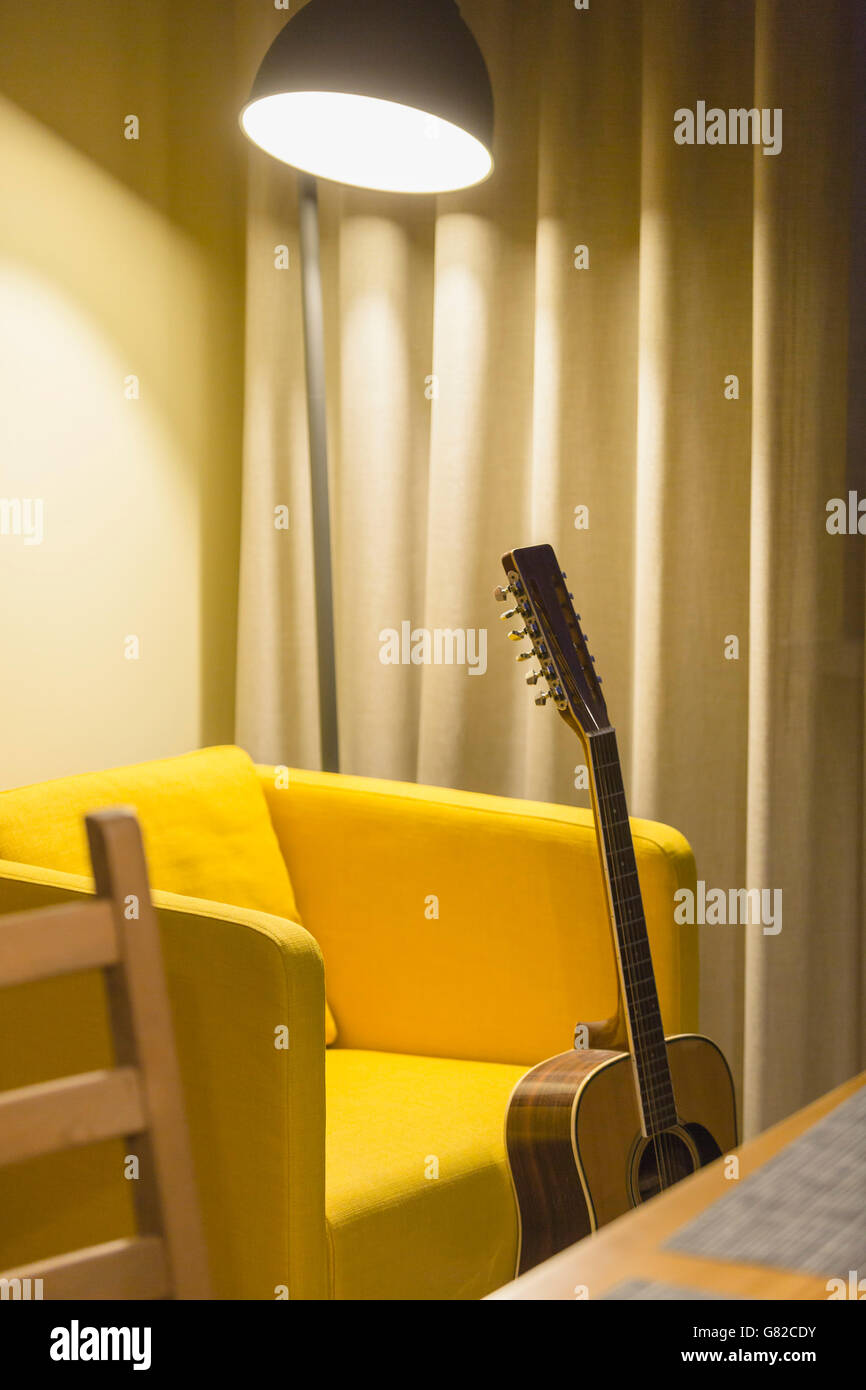 Akustische Gitarre gegen gelbe Stuhl zu Hause Stockfoto