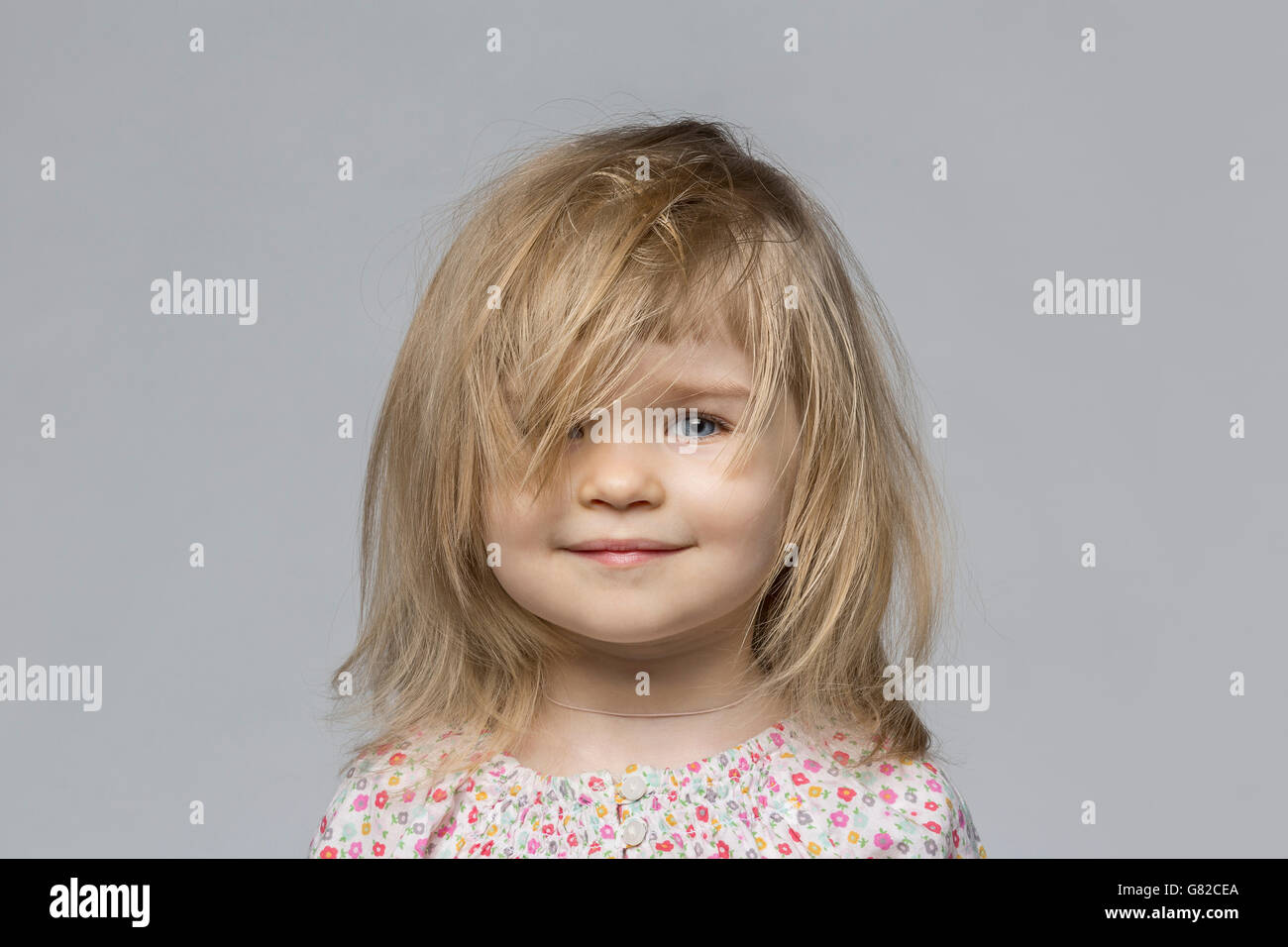 Porträt von lächelndes Mädchen mit zerzausten Haaren vor grauem Hintergrund Stockfoto