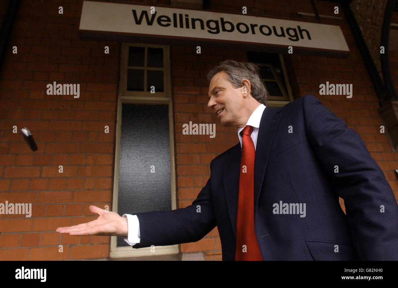 Der britische Premierminister Tony Blair wirft sein Mobiltelefon einem Helfer zu, während er am Bahnhof Wellingborough auf einen Zug wartet. Stockfoto