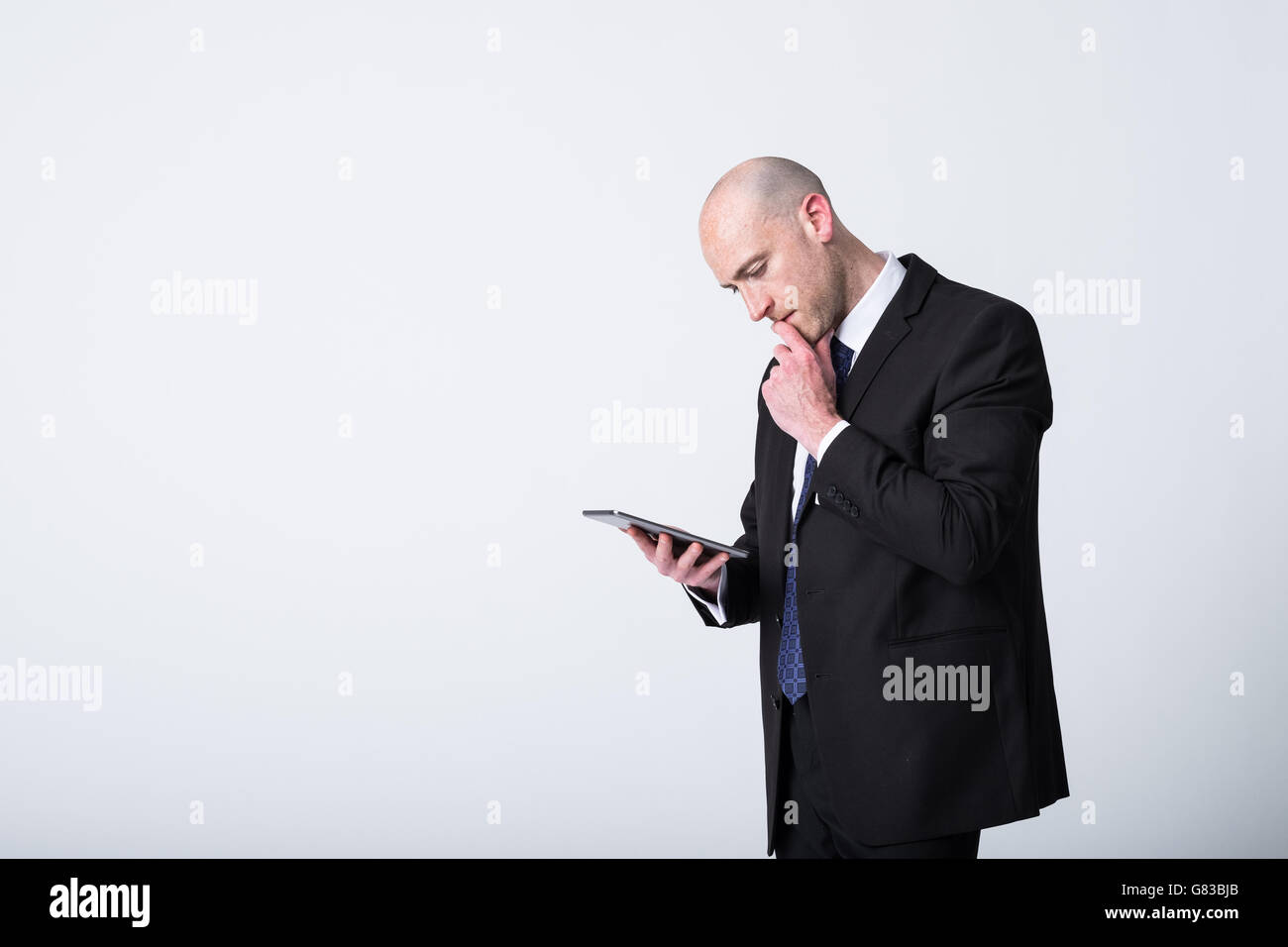 Ein klatschiger Geschäftsmann, der Daten und Informationen auf einem mobilen Tablet ansieht. Er hat einen verwirrten Blick und links vom Bild ist ein Kopierraum Stockfoto