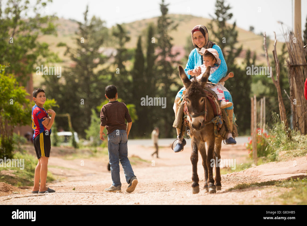 Eine Frau und ihr Kind reiten einen Esel auf einer unbefestigten Straße in das Dorf Ben Khili, Marokko. Stockfoto