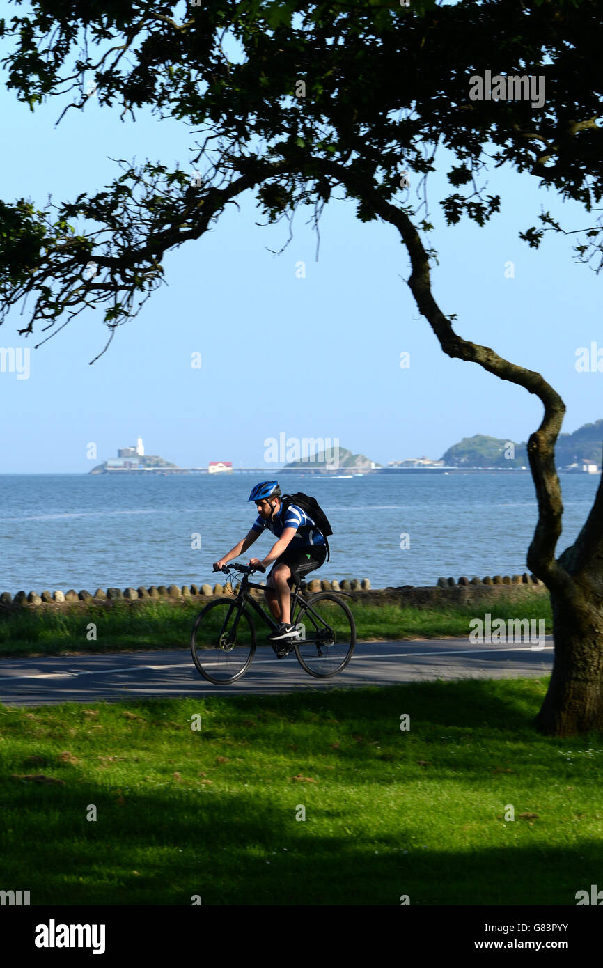 Radfahren auf Baum Küstenpfad am Mumnbles, Swansea Bay mit die Leuchtturm-Rettungsstation, Pier am Horizont bei Flut an einem blauen Tag gefüttert Stockfoto