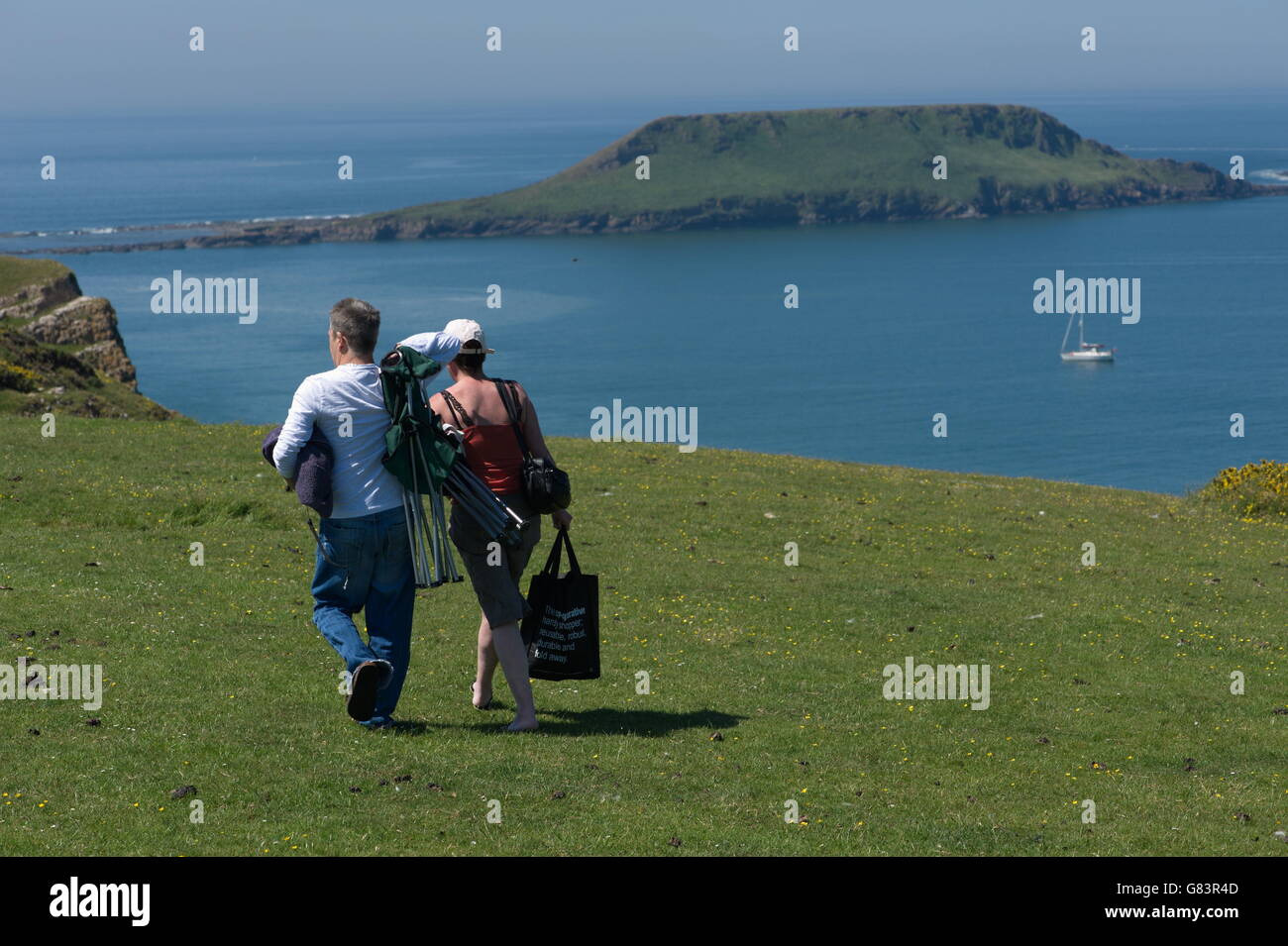 Paare, die auf Klippe Rhossili Bay. Eine Yacht liegt in der Bucht mit Wurm Kopf Hintergrund verankert Stockfoto