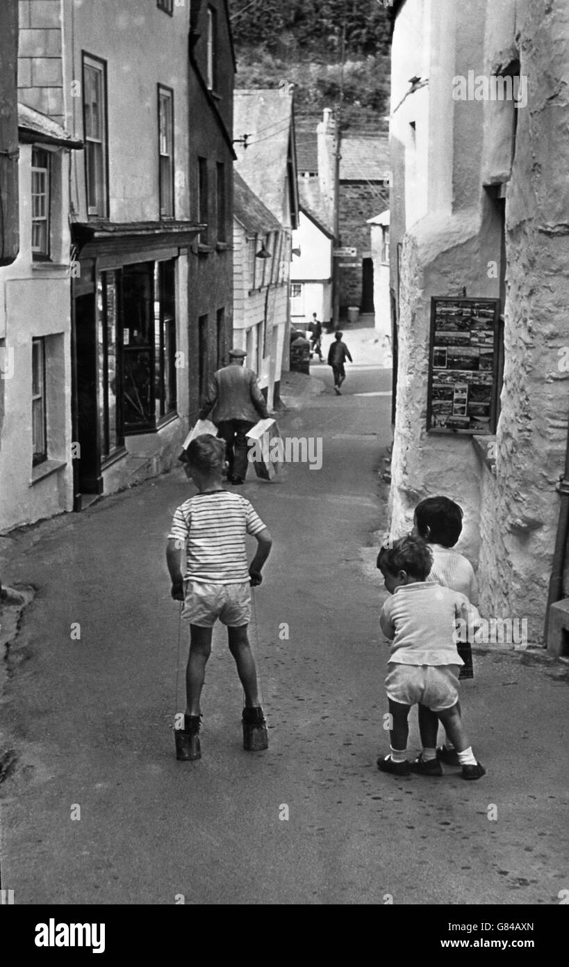 Ein kleiner Junge verwendet Blechdosen als Stelzen, während Kinder in Port Isaac, Cornwall, eine kleine Gasse spielen. Stockfoto