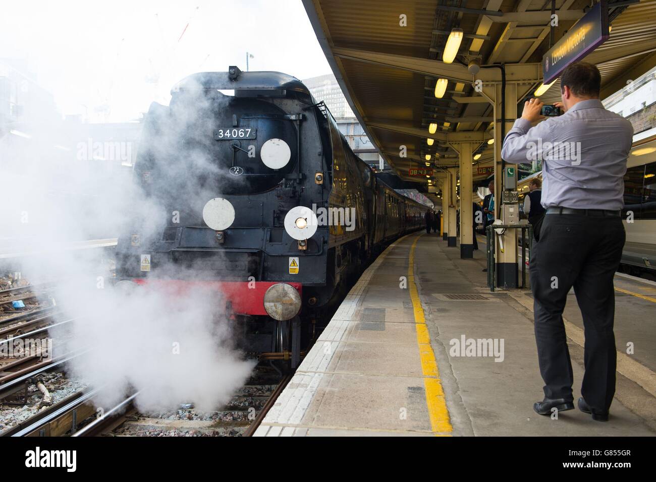 Ein Pendler macht ein Foto von 'Tangmere', einer Dampflokomotive der Battle of Britain-Klasse Pacific 4-6-2 von 1947, die den Dorset Coast Express Zug nach Weymouth am Bahnhof Victoria, London, zieht. Stockfoto