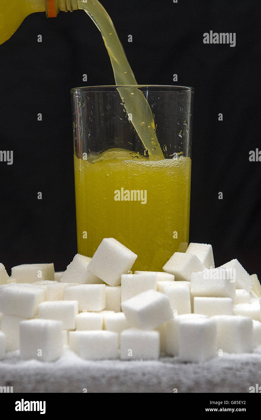 Ein von Zuckerwürfeln umgebenes, orangefarbenes Getränk, das zuckerhaltige Getränke trinkt, könnte laut Forschung fast 8,000 Fälle von Typ-2-Diabetes pro Jahr verursachen. Stockfoto