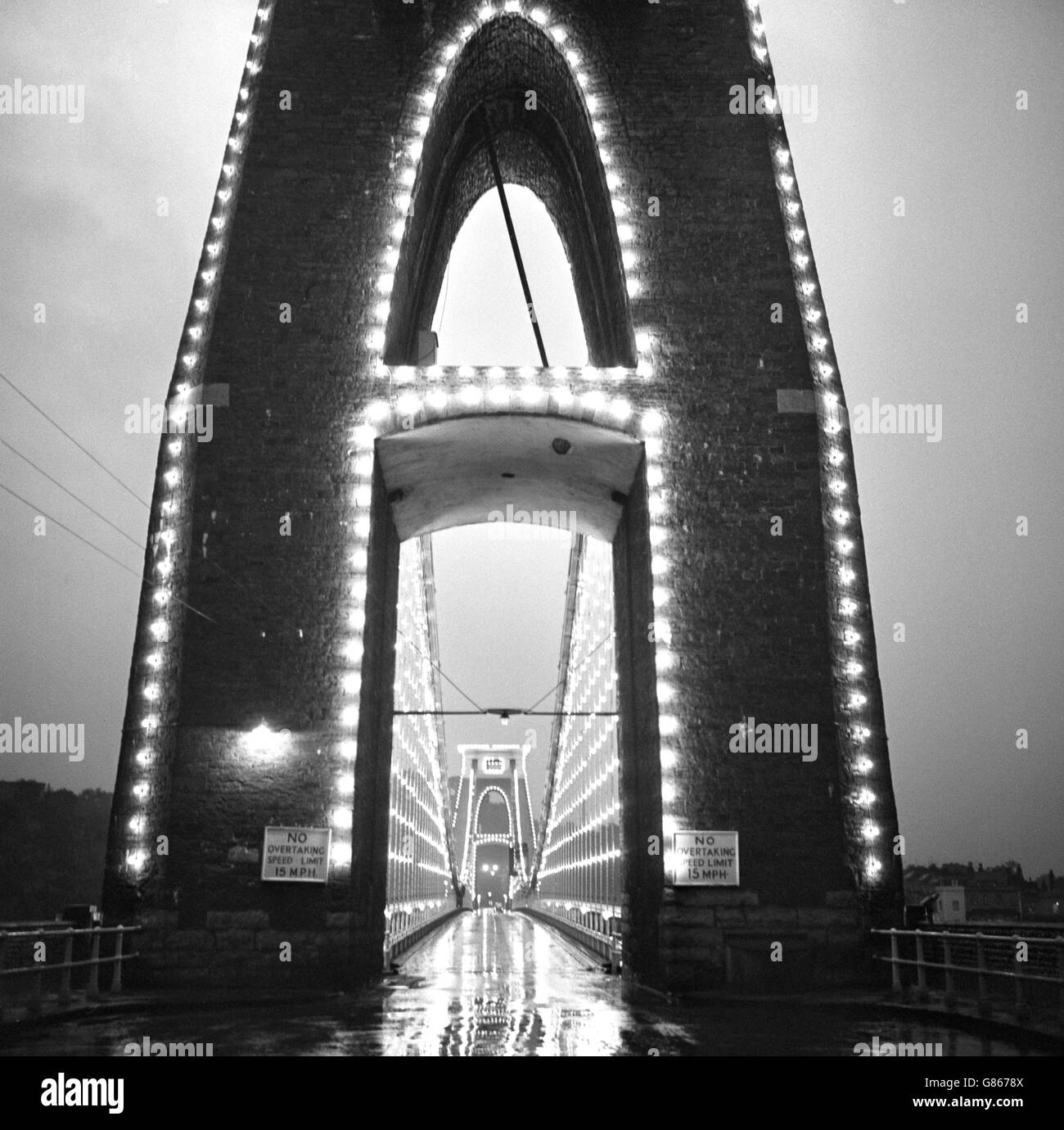 Blick vom Fahrer auf die Clifton Suspension Bridge, die im August und September in der Abenddämmerung beleuchtet wird. Stockfoto