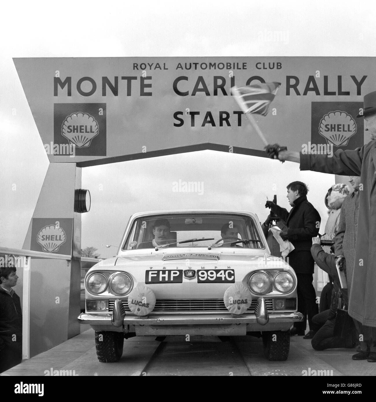 Die Triumph 2000 mit einem Crewet von Simo Lampinen (Fahren) und Jyrki Ahava aus Finnland startet auf dem Vorplatz des Forte's Excelsior Hotel am Flughafen London, einem der 39 Fahrzeuge, die bei der Rallye Monte Carlo in London starten. AK Stevenson, ehemaliger Sekretär des Scottish Royal Automobile Club, lässt die Flagge von Union Jack fallen. Stockfoto