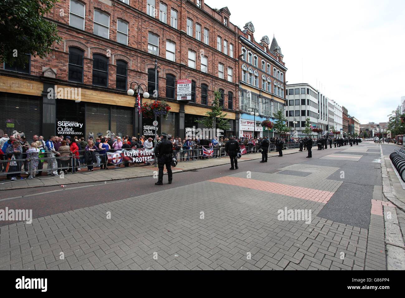 PSNI-Offiziere sehen sich an, wie Menschenmengen auf die Ankunft einer umstrittenen republikanischen Parade und der damit verbundenen loyalistischen Proteste warten. Stockfoto PSNI-Offiziere sehen sich an, wie Menschenmengen auf die Ankunft einer umstrittenen republikanischen Parade und der damit verbundenen loyalistischen Proteste warten. Stockfoto