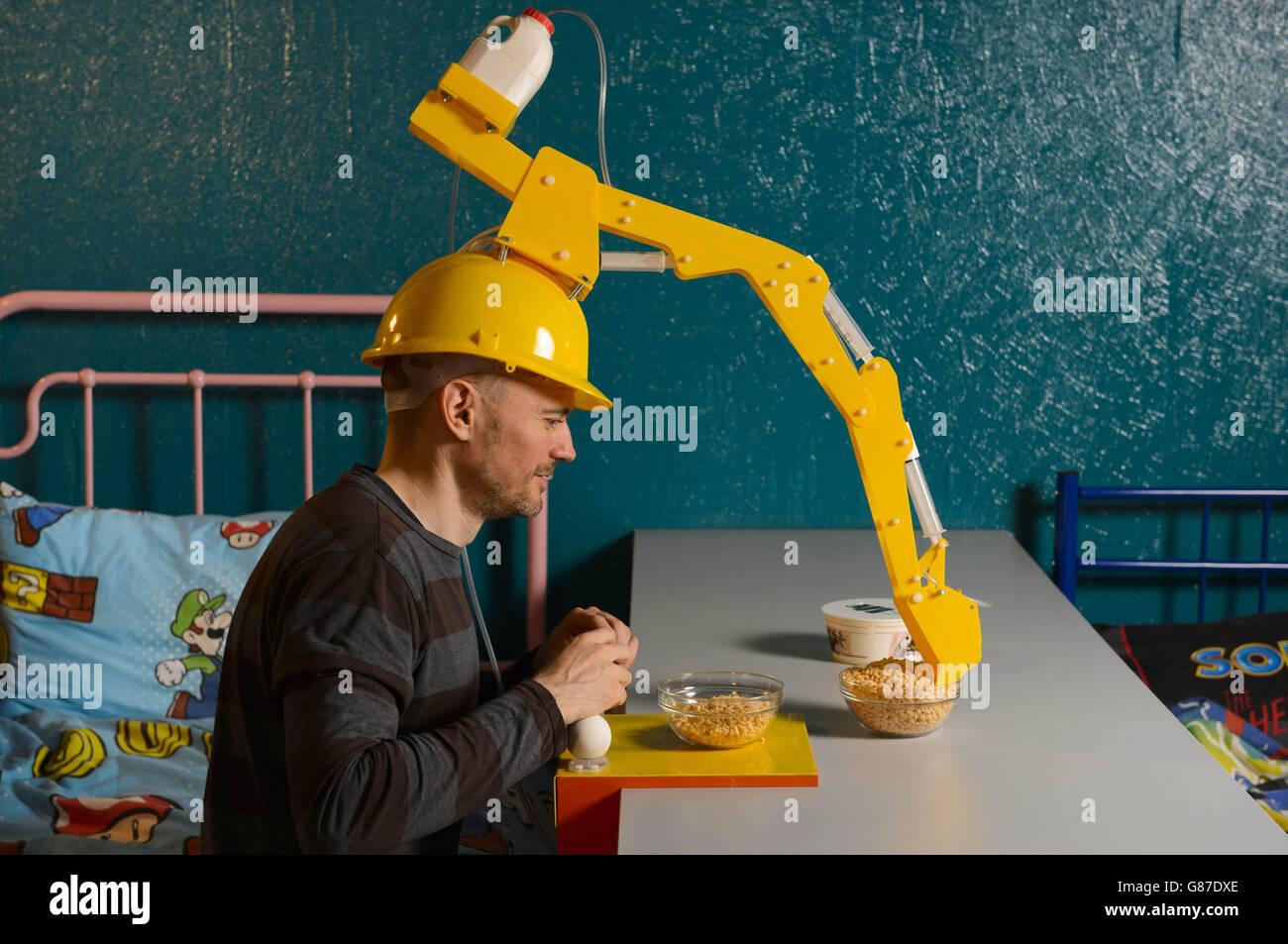 Der Künstler und Erfinder Dominic Wilcox zeigt sein neuestes Gadget, das 'Crane Head Cereal Serving Device', aus der Kellogg's Wearable Brek Kollektion, im Cereal Killer Cafe in Camden, London. Stockfoto