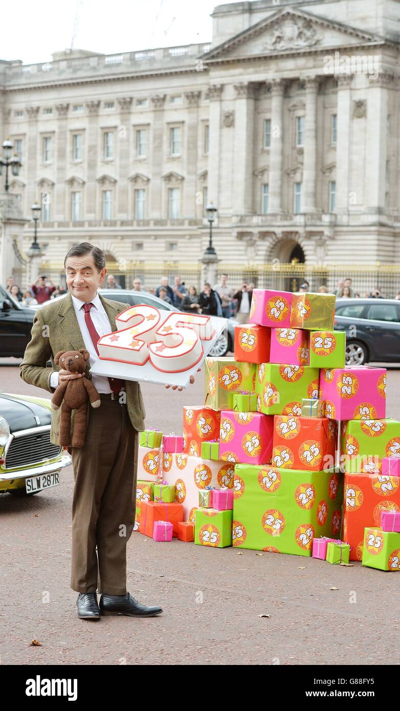 Mr Bean, gespielt von Rowan Atkinson, feiert den 25. Geburtstag der Figur in der Mall vor dem Buckingham Palace in London mit einem Kuchen und seinem Teddybären. Stockfoto