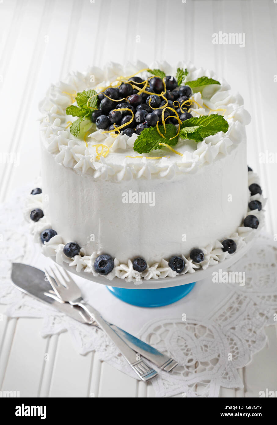Heidelbeer-Kuchen mit Vanille Zuckerguss verziert mit Heidelbeeren, Zitrone Zest und Minze Blätter. Stockfoto