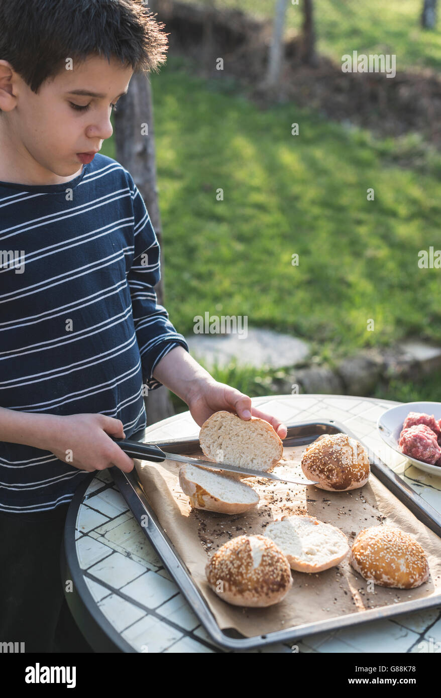 Junge-schneiden-Burger-Brötchen im Garten Stockfoto