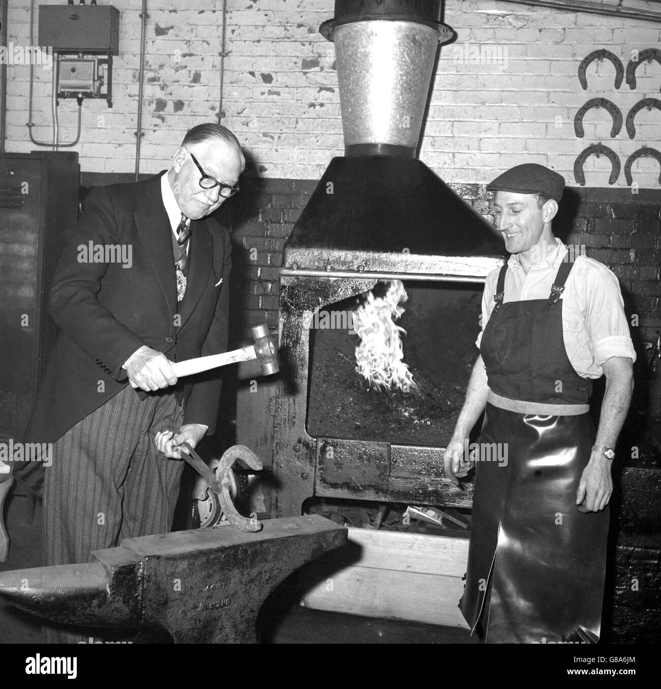Sir Lionel Denny, Londons Oberbürgermeister, formt unter den zustimmenden Augen von Joe Tucker ein Hufeisen auf dem Amboss während seines Besuchs in Whitbread Stables in der Garrett Street, Clerkenwell. In den Ställen sah er die sechs Brauereipferde, die seinen Trainer im vergangenen November auf der Lord Mayor's Show zogen. Stockfoto Sir Lionel Denny, Londons Oberbürgermeister, formt unter den zustimmenden Augen von Joe Tucker ein Hufeisen auf dem Amboss während seines Besuchs in Whitbread Stables in der Garrett Street, Clerkenwell. In den Ställen sah er die sechs Brauereipferde, die seinen Trainer im vergangenen November auf der Lord Mayor's Show zogen. Stockfoto