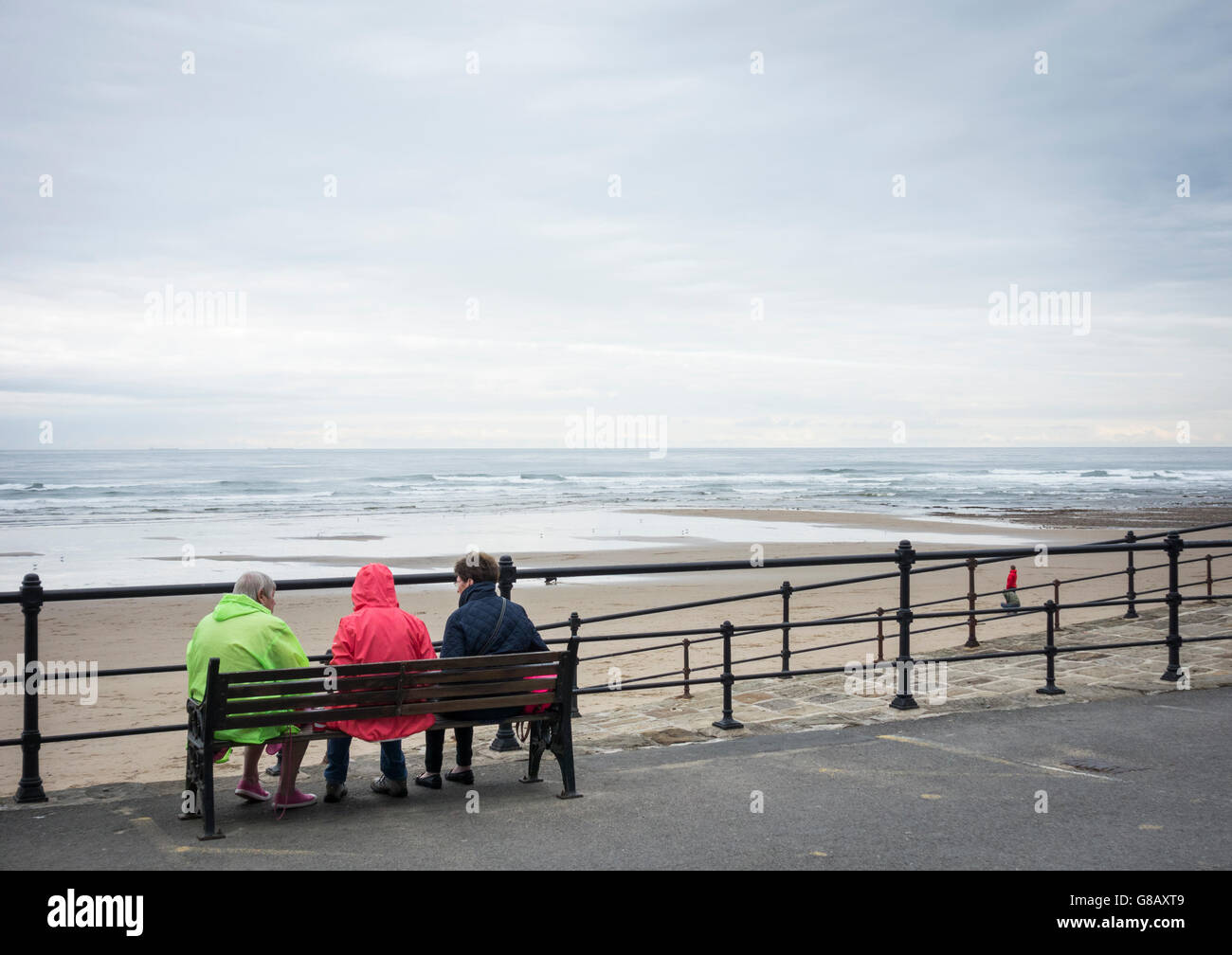 Rückansicht der drei Reife Frauen sitzen auf der Bank mit Blick auf Strand, an einem grauen, kalten Tag in England. UK Stockfoto