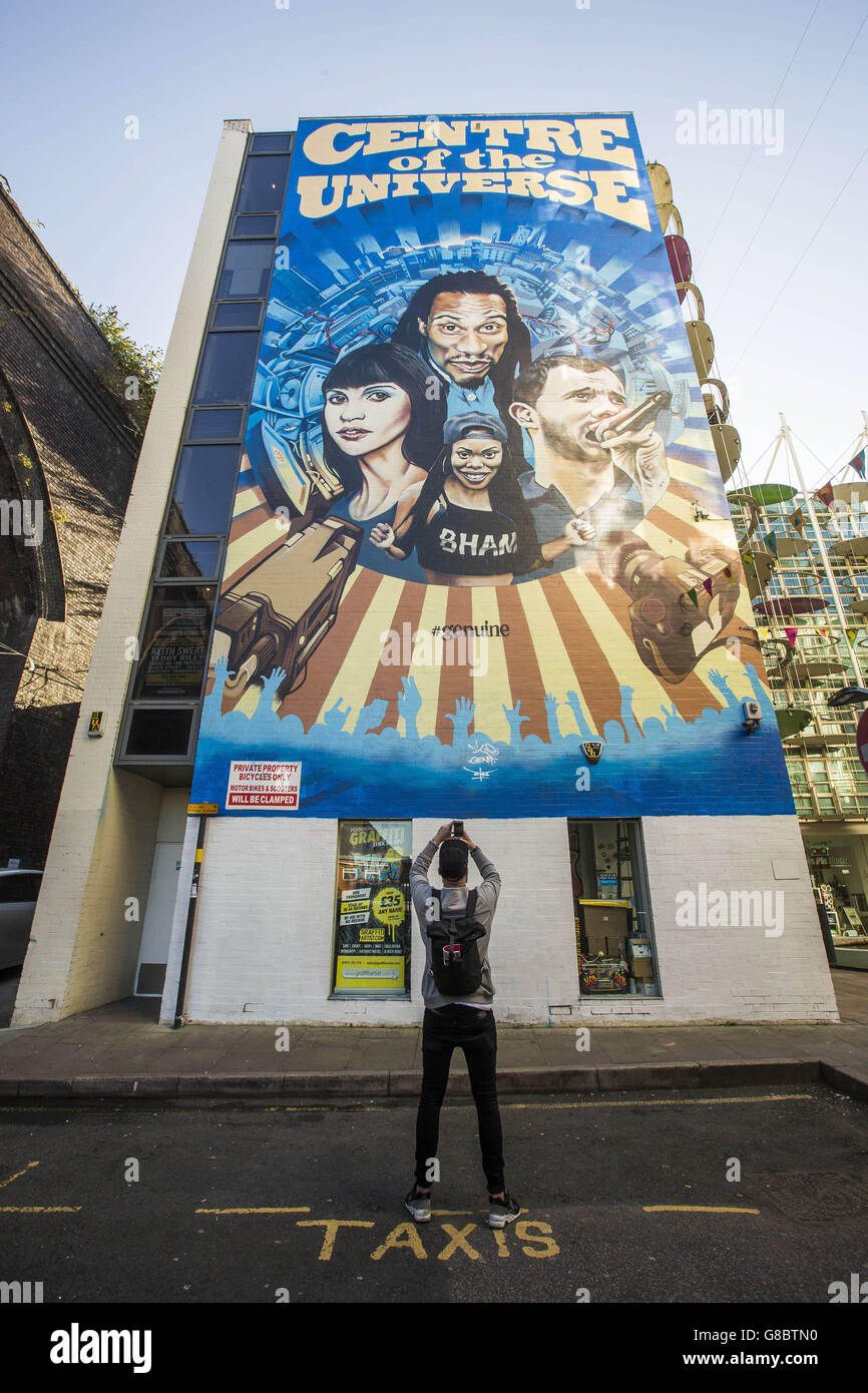 Eine Person macht ein Bild von einem sechsstöckigen hohen Stück Street Art mit Birmingham geboren Koryphäen &ETH; Der Dichter Benjamin Zephaniah, der Musiker Mike Skinner, Rap-Künstler Lady Leshurr und die Schauspielerin Felicity Jones werden vor der Custard Factory in Birmingham von Chu gemalt, um das größte Street-Art-Projekt Großbritanniens zu starten, das von 'Get it Right from a Genuine Site' in Auftrag gegeben wurde. Stockfoto