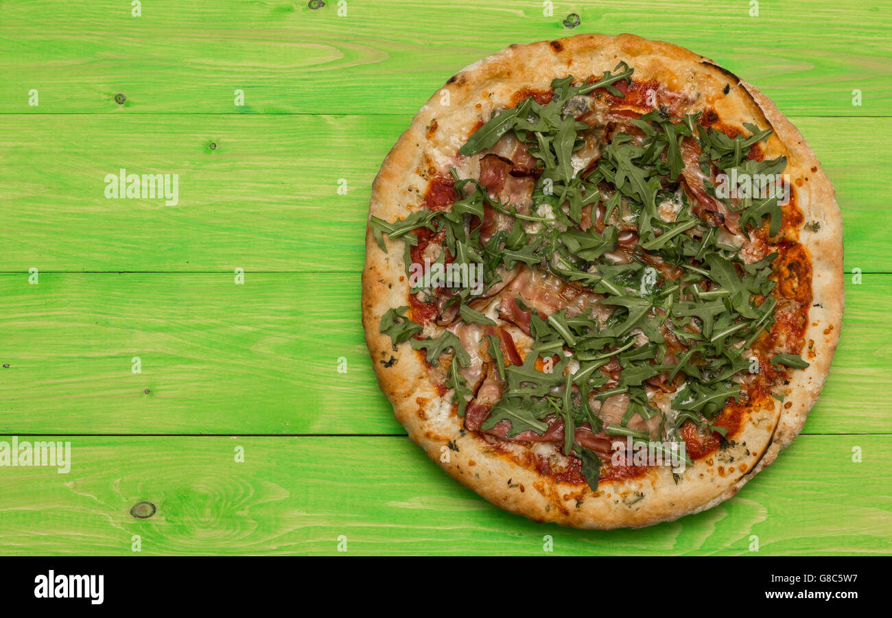 Pizza mit Schinken, Gorgonzola und frischem Rucola-Salat auf einem grünen Holztisch Stockfoto