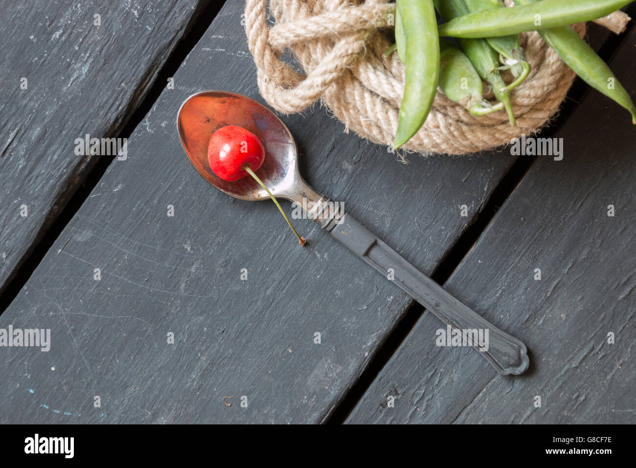 Löffel mit einer Kirsche und grünen Bohnen Stockfoto