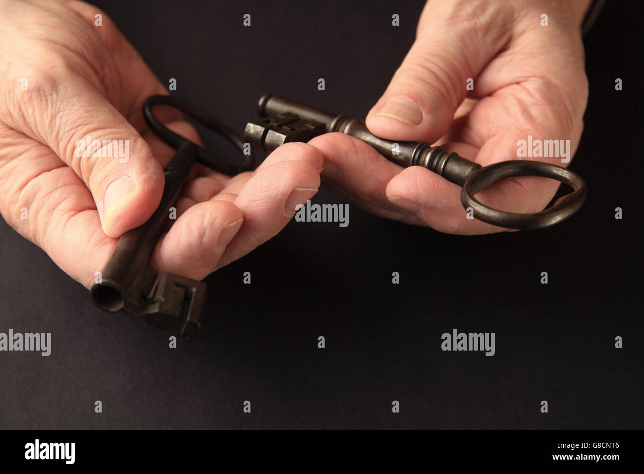 Älterer Mann hat zwei große, alte Schlüssel auf eine schwarze Fläche mit Textfreiraum. Stockfoto