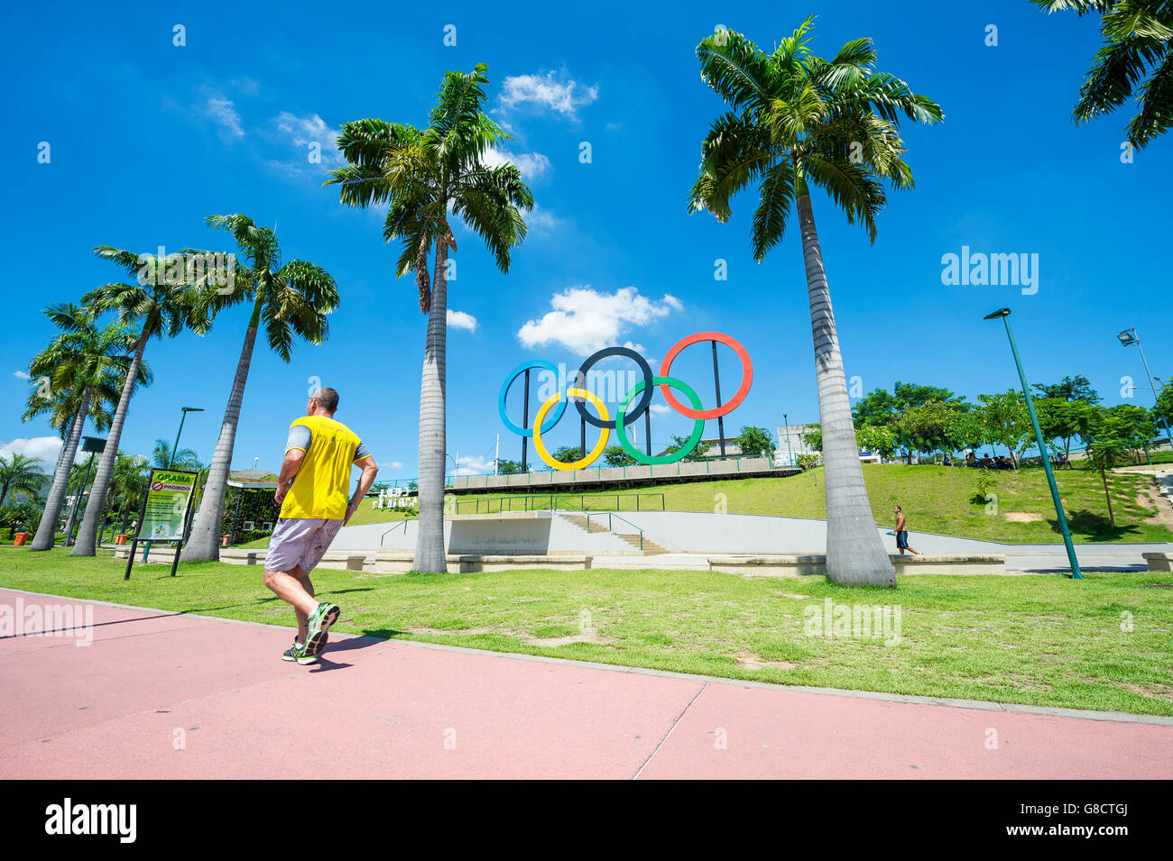 RIO DE JANEIRO - 18. März 2016: Ein Jogger passiert vor Olympischen Ringe für die Olympischen Sommerspiele 2016 in einem Park installiert. Stockfoto
