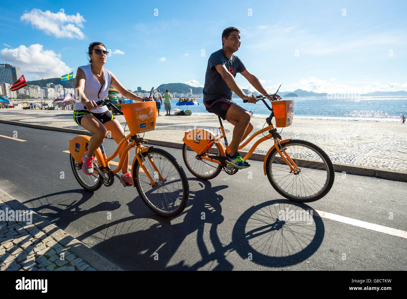 RIO DE JANEIRO - 20. März 2016: Brasilianer Fahrt orange Bike-sharing Fahrräder gesponsert von Itau Bank direkt am Copacabana Strand. Stockfoto