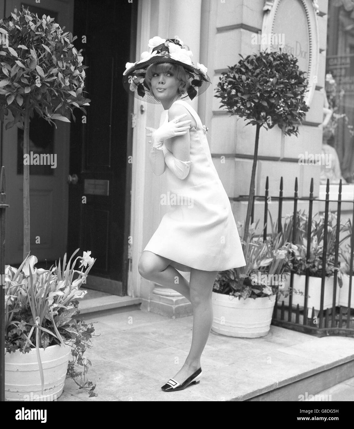 Ein weißes Seidenkleid mit einem Saum weit über den Knien wurde in London in der Frühjahr 1966 Modekollektion von Christian Dior-London gesehen. Der schwarze Hut ist mit Blumen verziert. Stockfoto