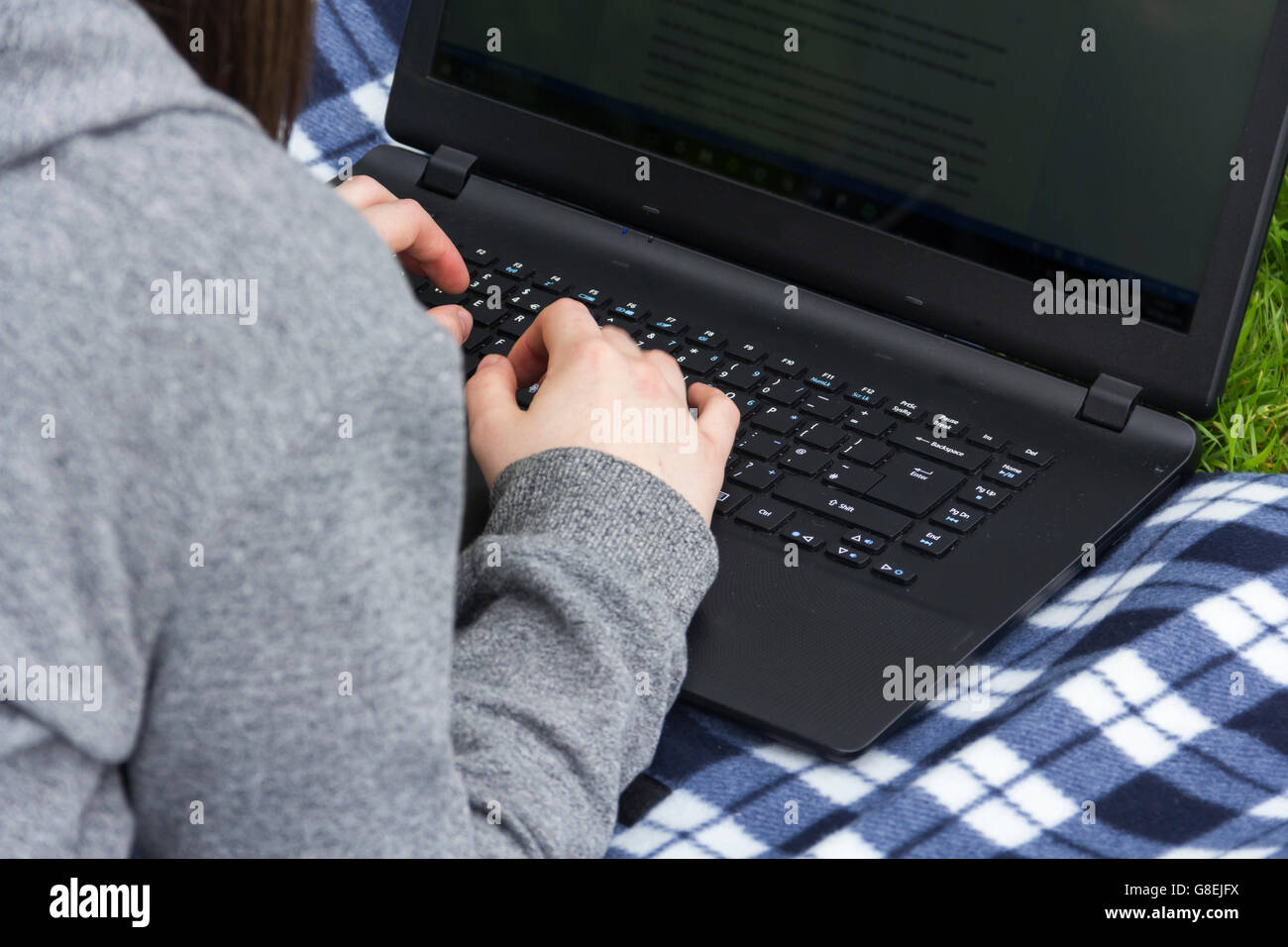 Junge Frau, Erwachsene oder späten Teens Student, Bauchlage auf einer Picknickdecke auf dem Rasen mit Blick auf ihr Smartphone und Laptop. Stockfoto