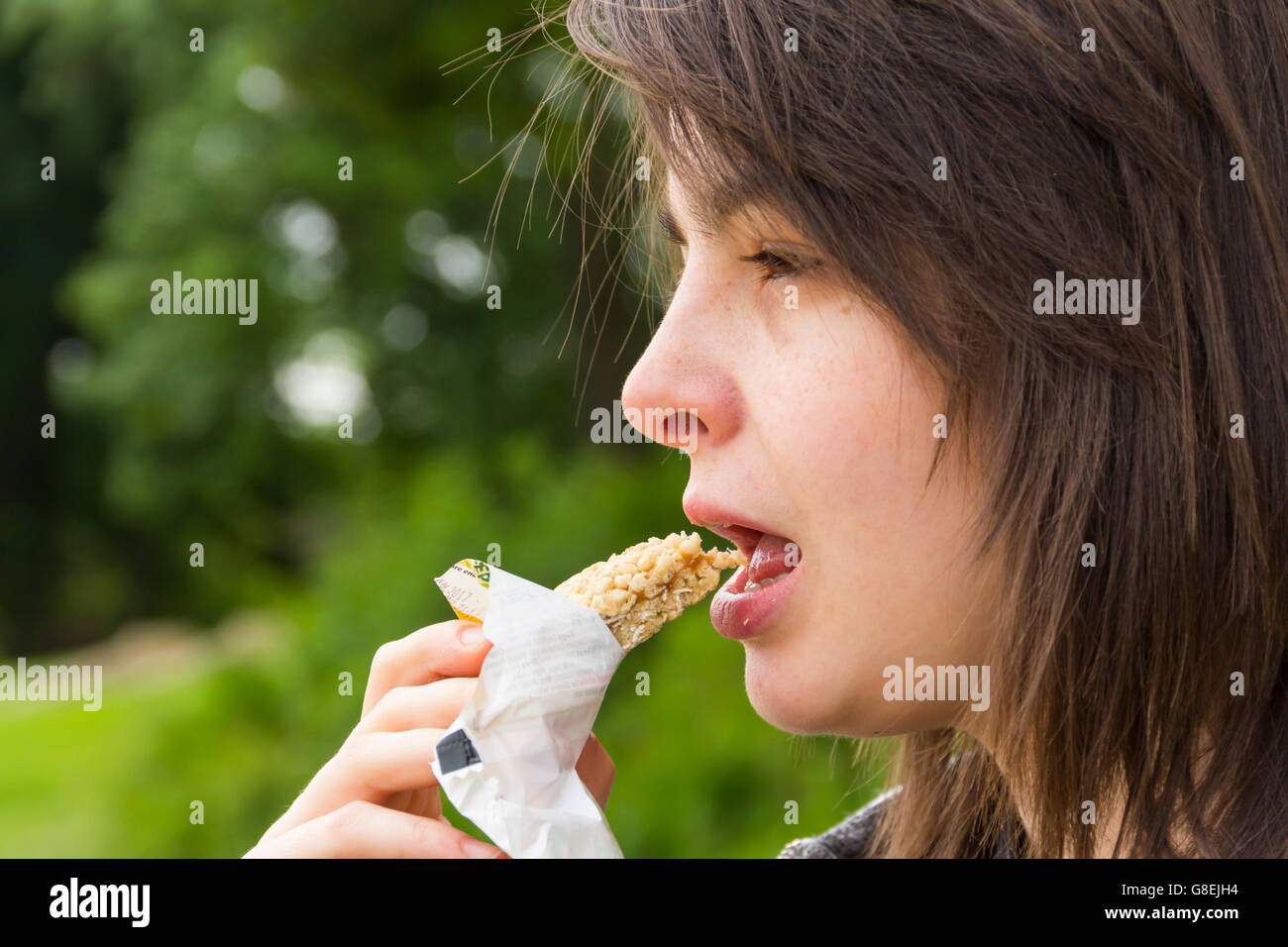 Junge Frau, Erwachsene oder späten Teens, Kopfschuss Seitenansicht in einem Park einen Müsliriegel zu essen. Stockfoto