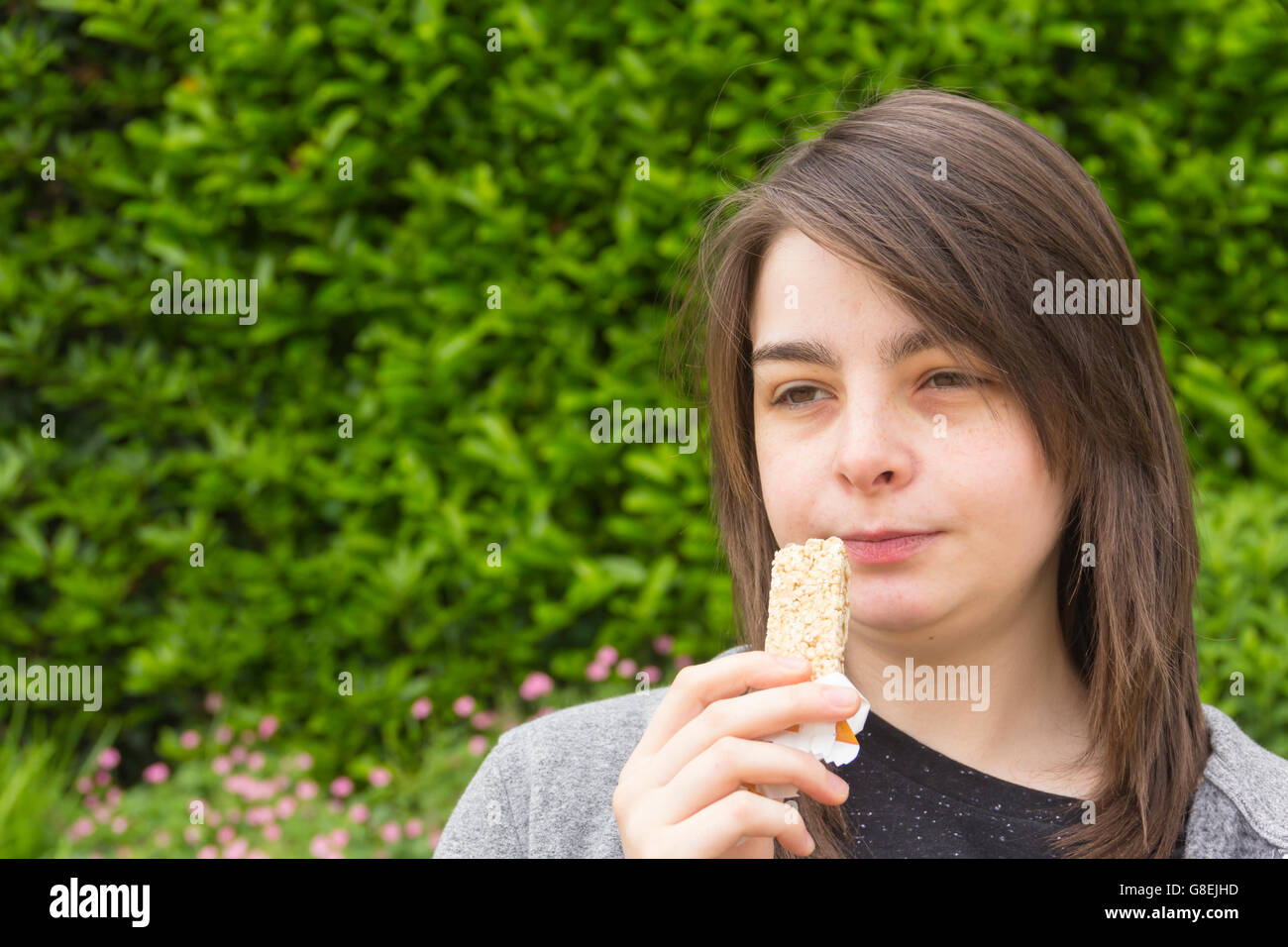 Junge Frau, Erwachsene oder späten Teens, Kopfschuss in einem Park einen Müsliriegel zu essen. Stockfoto