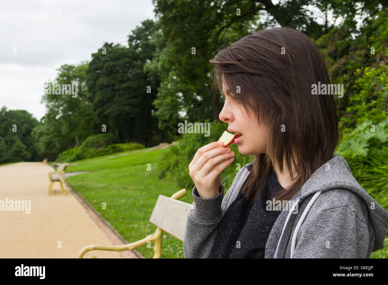 Junge Frau, Erwachsene oder späten Teens, sitzen im Park ein Stück Apfel zu essen. Stockfoto