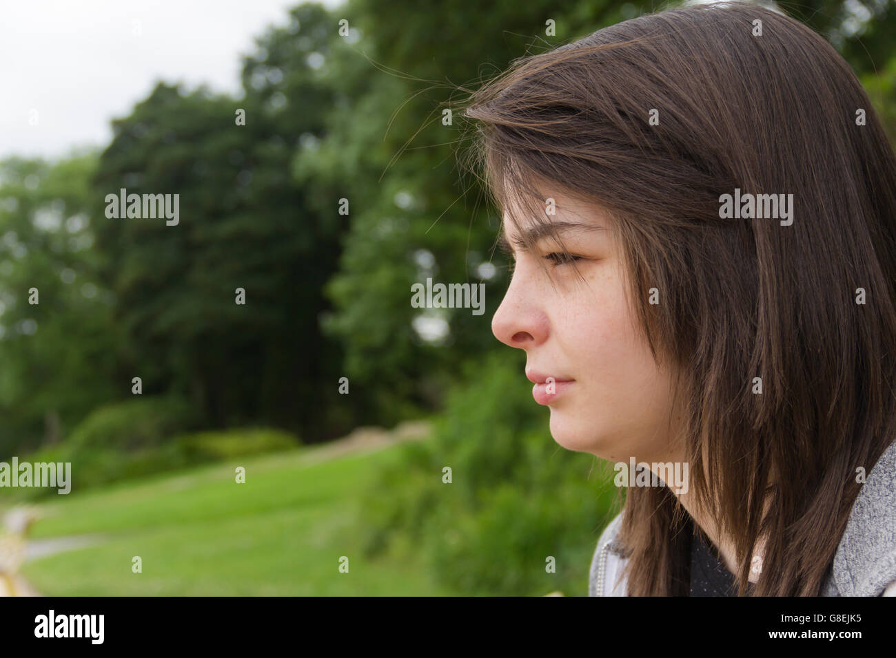 Junge Frau, Erwachsene oder späten Teens, sitzen im Park mit einem feierlichen oder neutralen Ausdruck auf ihrem Gesicht. Stockfoto